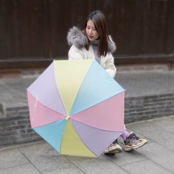 Woman sitting outdoors holding a Large Pastel Rainbow Umbrella with Pink, Yellow, Blue, and Lavender Panels