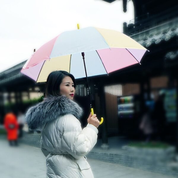 Woman in white winter coat holding colorful rainbow umbrella.