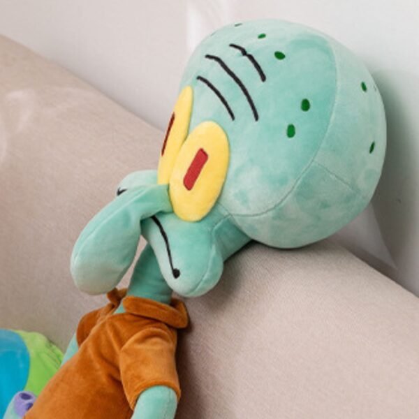 Squidward Tentacles plush toy from SpongeBob SquarPants, featuring his teal head, large nose, and orange shirt, leaning on a beige couch.