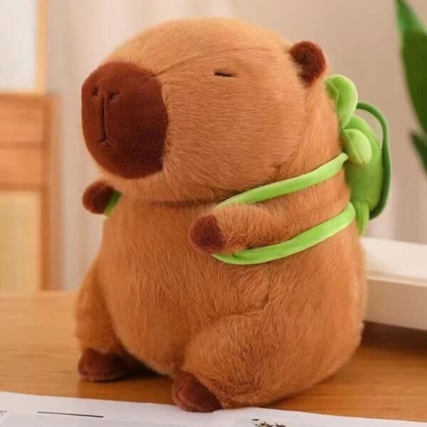 Cute brown plush capybara toy with green turtle tied on its back, sitting on a wooden table.